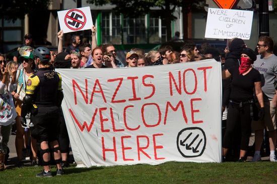 EDITORS NOTE: Graphic content / Antifa members hold a sign denouncing Nazis along a road at a waterfront park in downtown Portland, Oregon September 10. 2017. .Several hundred protesters descended in to downtown Portland to oppose the right-wing group. / AFP PHOTO / Natalie Behring (Photo credit should read NATALIE BEHRING/AFP/Getty Images)